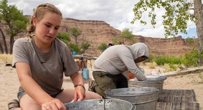 Two people work with buckets as part of a service project. They are in a desert environment. 